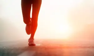 Biegaczka w świetle wschodzącego słońca. Jej nogi w legginsach i butach sportowych są w ruchu. To jak test coopera, gdzie każdy krok się liczy.