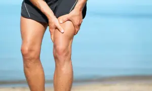 Ból w udzie, gdzie znajduje się mięsień czworogłowy. Mężczyzna trzyma się za nogę na plaży.
