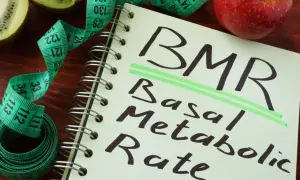 Notatnik z napisem BMR (Basal Metabolic Rate), obok jabłko, kiwi i miarka krawiecka. Obliczenia BMR, jak wzór Harrisa Benedicta, pomagają zrozumieć metabolizm.