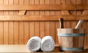 Drewniana sauna z dwoma ręcznikami i wiadrem. Odpoczynek w saunie to relaks i oczyszczenie.