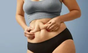 Kobieta z "skinny fat" sylwetką, chwytająca fałd skóry na brzuchu.