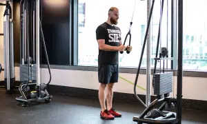 Mężczyzna wykonuje ćwiczenie triceps extension na maszynie typu cable cross.