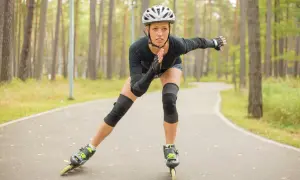 Kobieta w kasku i ochraniaczach jedzie na rolkach po leśnej ścieżce, spalając kalorie.