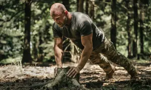 Mężczyzna w leśnej scenerii wykonuje pompki na pniu. To trening siłowy, który jest częścią jego pasji do bushcraftu.