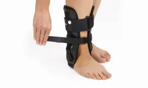 Dłoń zapina czarną ortezę stawu skokowego na nodze.
