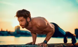 Mężczyzna wykonuje pompki na biceps przy zachodzie słońca.