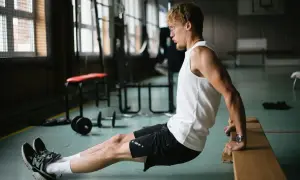 Mężczyzna wykonuje ćwiczenie dipy na triceps, opierając dłonie o ławkę.