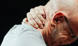Mężczyzna masuje kark, odczuwając silny ból szyi przy skręcaniu głowy.