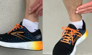 Biegacz dotyka łydki, być może z powodu bólu shin splints. Na stopach ma czarne buty biegowe Brooks z pomarańczowymi sznurówkami.
