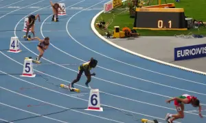 Biegaczki na 400 m walczą o rekord świata. Na bieżni widać zawodniczki w akcji, numery torów i zegar z wynikiem 0.1.