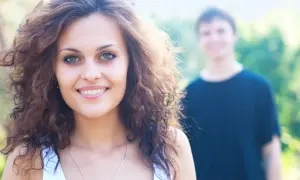 Uśmiechnięta kobieta z kręconymi włosami, w tle mężczyzna. Ich radość to czyste endorfiny.