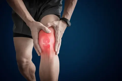 Ból w stawie kolanowym. Czerwony obszar podkreśla bolesne miejsce na kolanie, które osoba trzyma rękami.