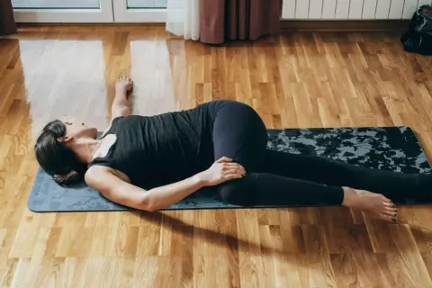 Kobieta ćwiczy na macie, wykonując skręt tułowia. Ćwiczenie to pomaga pozbyć się tzw. wdowi garb.