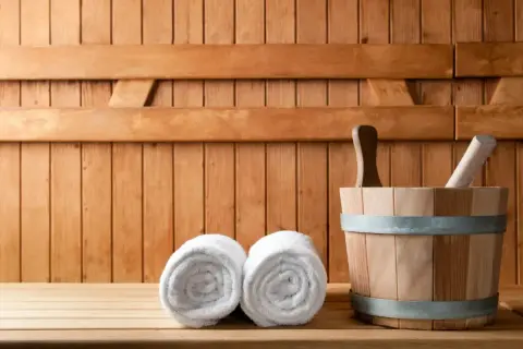 Drewniana sauna z dwoma ręcznikami i wiadrem. Odpoczynek w saunie to relaks i oczyszczenie.