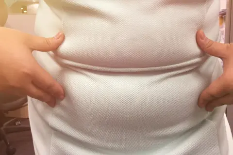 Dłonie ściskają białą koszulkę, uwydatniając zaokrąglony brzuch, który może być oznaką brzucha hormonalnego.