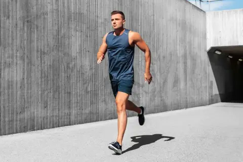 Mężczyzna w sportowym stroju wykonuje rozgrzewkę przed bieganiem, biegnąc wzdłuż betonowej ściany.
