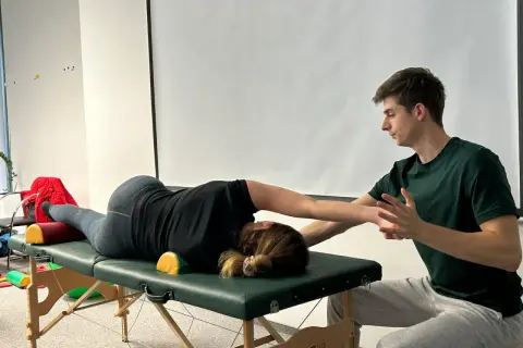 Fizjoterapeuta pomaga pacjentce w ćwiczeniach na stole rehabilitacyjnym, wspierając jej ruchy.