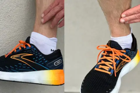 Biegacz dotyka łydki, być może z powodu bólu shin splints. Na stopach ma czarne buty biegowe Brooks z pomarańczowymi sznurówkami.