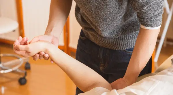 Fizjoterapeuta bada rękę pacjentki, oceniając bliznę po operacji cieśni nadgarstka.