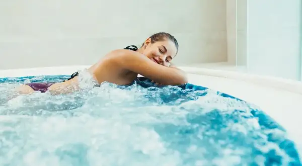 Kobieta zrelaksowana w wannie z hydromasażem, ciesząca się bąbelkami i ciepłą wodą.