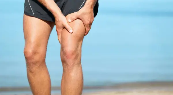 Ból w udzie, gdzie znajduje się mięsień czworogłowy. Mężczyzna trzyma się za nogę na plaży.