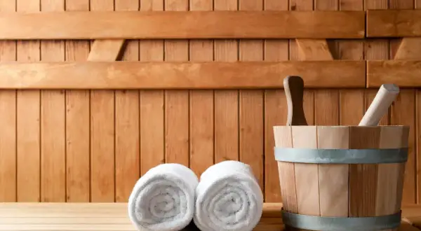 Drewniana sauna z dwoma ręcznikami i wiadrem. Odpoczynek w saunie to relaks i oczyszczenie.