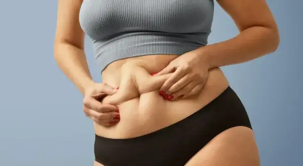 Kobieta z "skinny fat" sylwetką, chwytająca fałd skóry na brzuchu.