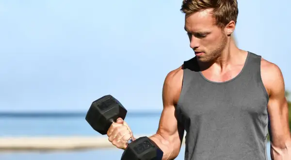 Mężczyzna ćwiczy biceps z hantlem, zastanawiając się, ile serii na biceps w tygodniu da najlepsze efekty.