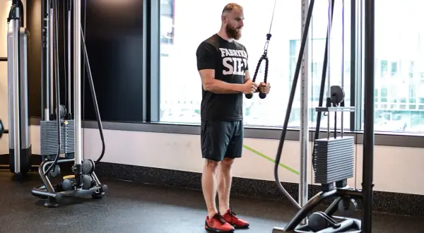 Mężczyzna wykonuje ćwiczenie triceps extension na maszynie typu cable cross.