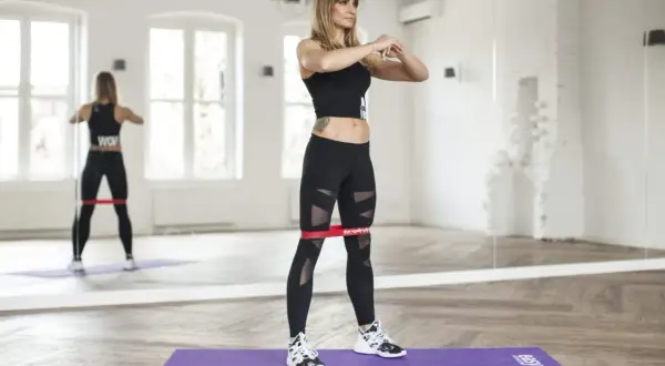 Kobieta wykonuje ćwiczenia z gumami mini band, wzmacniając mięśnie nóg.