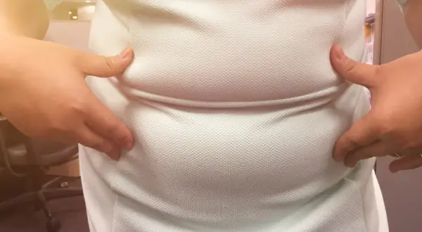 Dłonie ściskają białą koszulkę, uwydatniając zaokrąglony brzuch, który może być oznaką brzucha hormonalnego.