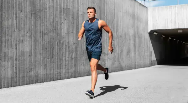 Mężczyzna w sportowym stroju wykonuje rozgrzewkę przed bieganiem, biegnąc wzdłuż betonowej ściany.