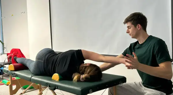 Fizjoterapeuta pomaga pacjentce w ćwiczeniach na stole rehabilitacyjnym, wspierając jej ruchy.