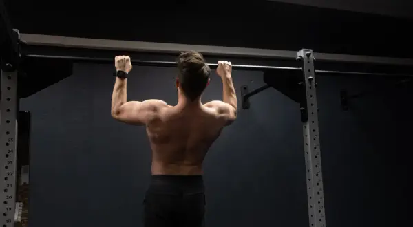 Mężczyzna wykonuje ćwiczenie pull up na drążku, budując siłę pleców i ramion.