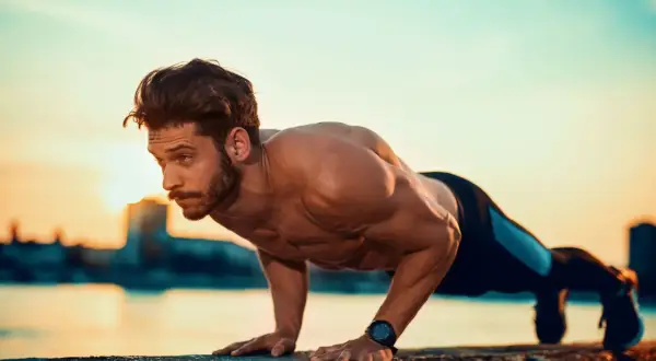 Mężczyzna wykonuje pompki na biceps przy zachodzie słońca.
