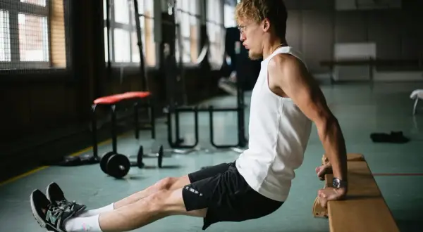 Mężczyzna wykonuje ćwiczenie dipy na triceps, opierając dłonie o ławkę.