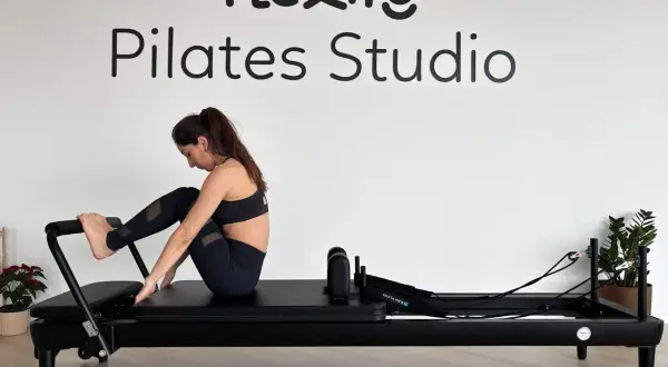 Kobieta ćwiczy na reformerze. Widoczne napisy "Flexity Pilates Studio". To dowód na pilates efekty po miesiącu.