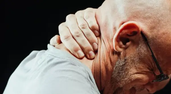 Mężczyzna masuje kark, odczuwając silny ból szyi przy skręcaniu głowy.