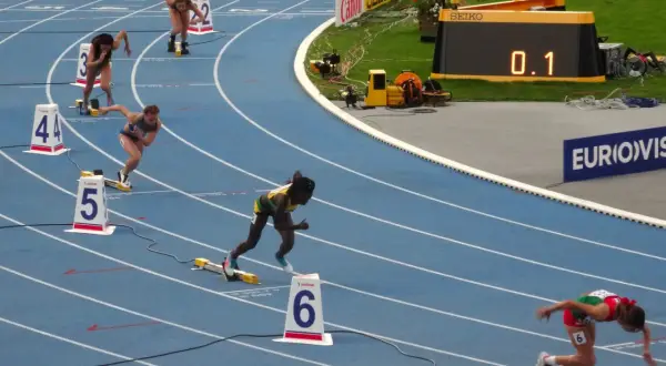 Biegaczki na 400 m walczą o rekord świata. Na bieżni widać zawodniczki w akcji, numery torów i zegar z wynikiem 0.1.