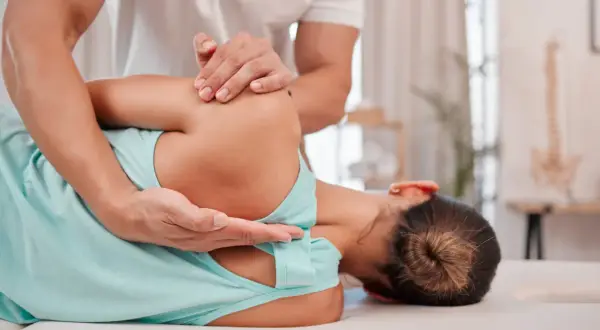 Fizjoterapeuta pomaga pacjentce zmagającej się z neurologiczne bóle mięśni, wykonując delikatny masaż barku.