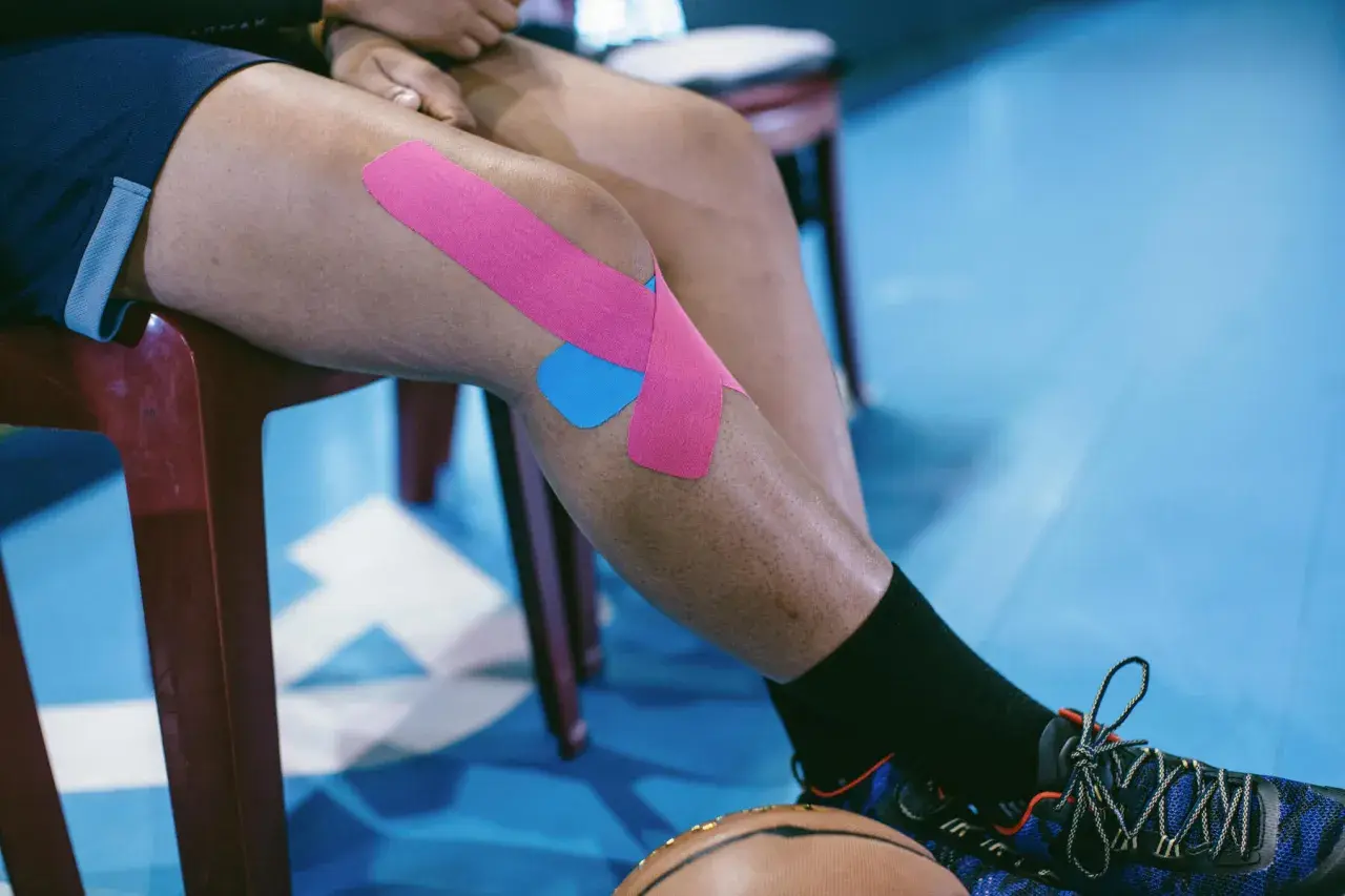Osoba z chondromalacją rzepki stosuje kinesiotaping. Różowe i niebieskie plastry na kolanie wspierają ćwiczenia.