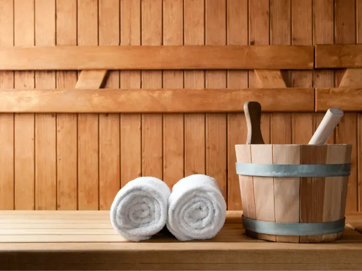 Drewniana sauna z dwoma ręcznikami i wiadrem. Odpoczynek w saunie to relaks i oczyszczenie.
