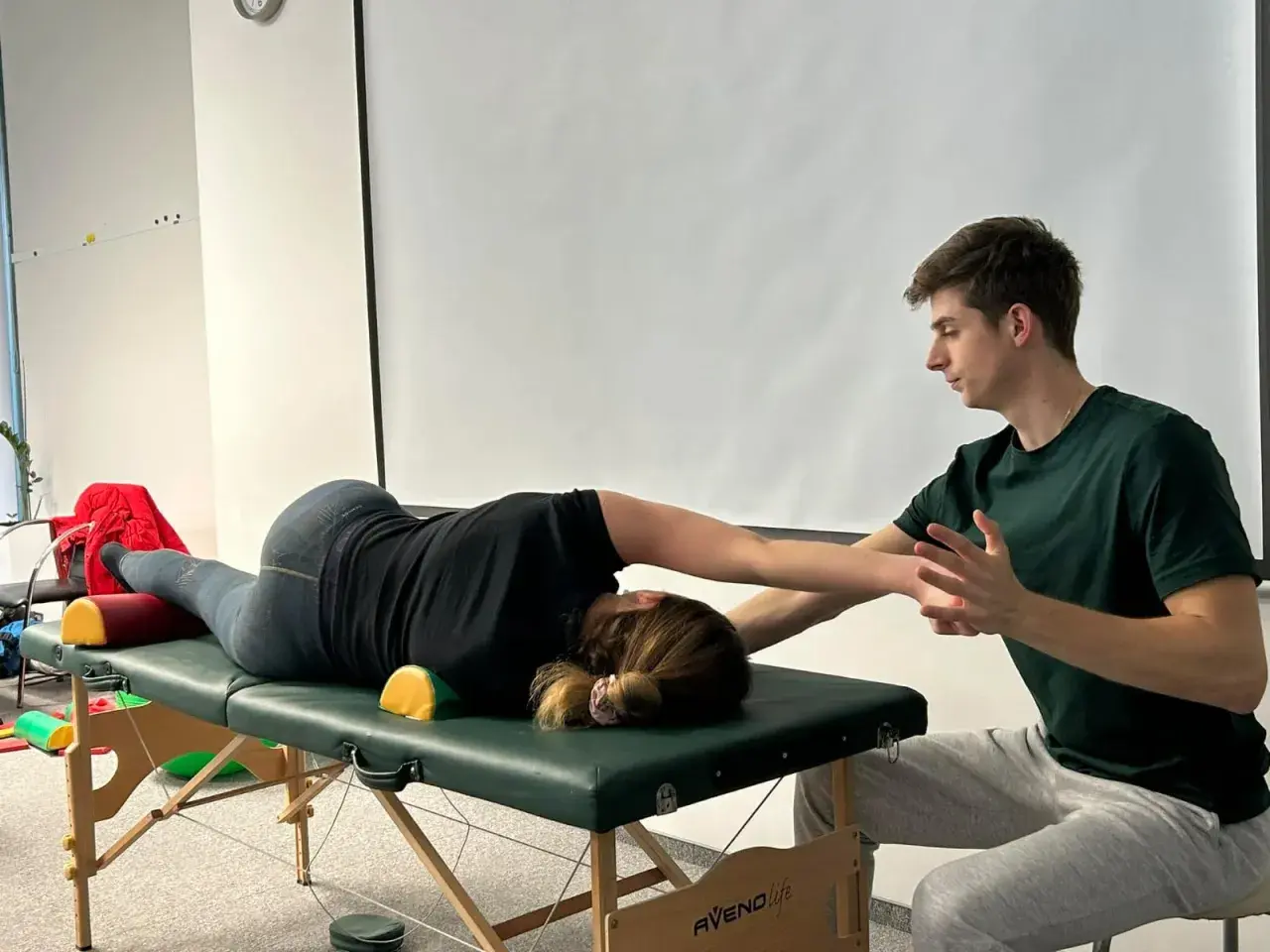 Fizjoterapeuta pomaga pacjentce w ćwiczeniach na stole rehabilitacyjnym, wspierając jej ruchy.