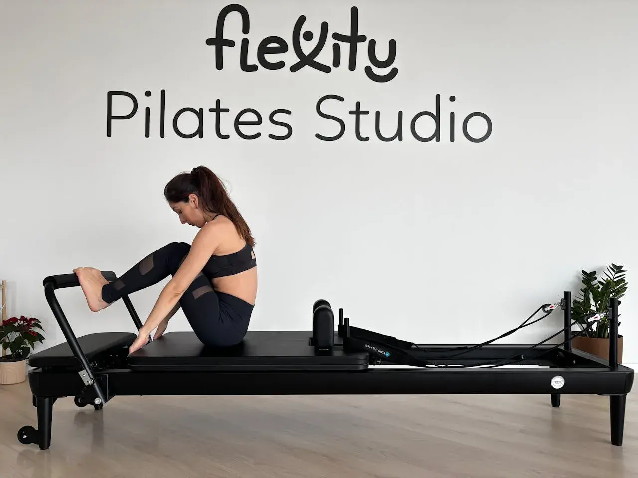 Kobieta ćwiczy na reformerze. Widoczne napisy "Flexity Pilates Studio". To dowód na pilates efekty po miesiącu.