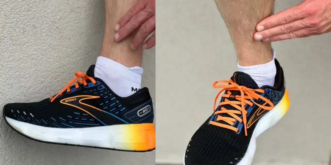 Biegacz dotyka łydki, być może z powodu bólu shin splints. Na stopach ma czarne buty biegowe Brooks z pomarańczowymi sznurówkami.