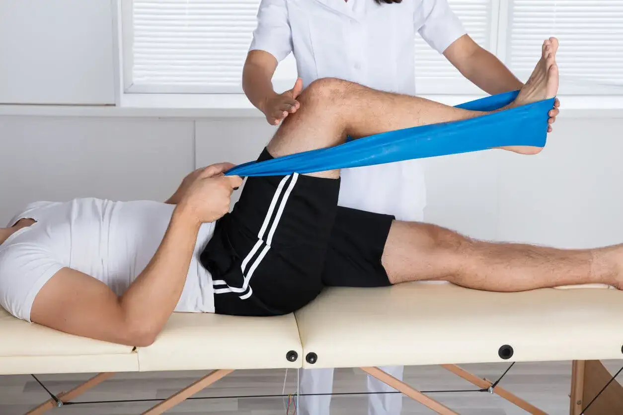 Fizjoterapeuta pomaga pacjentowi z gonartrozą kolana w ćwiczeniach z taśmą oporową, wzmacniając mięśnie uda.