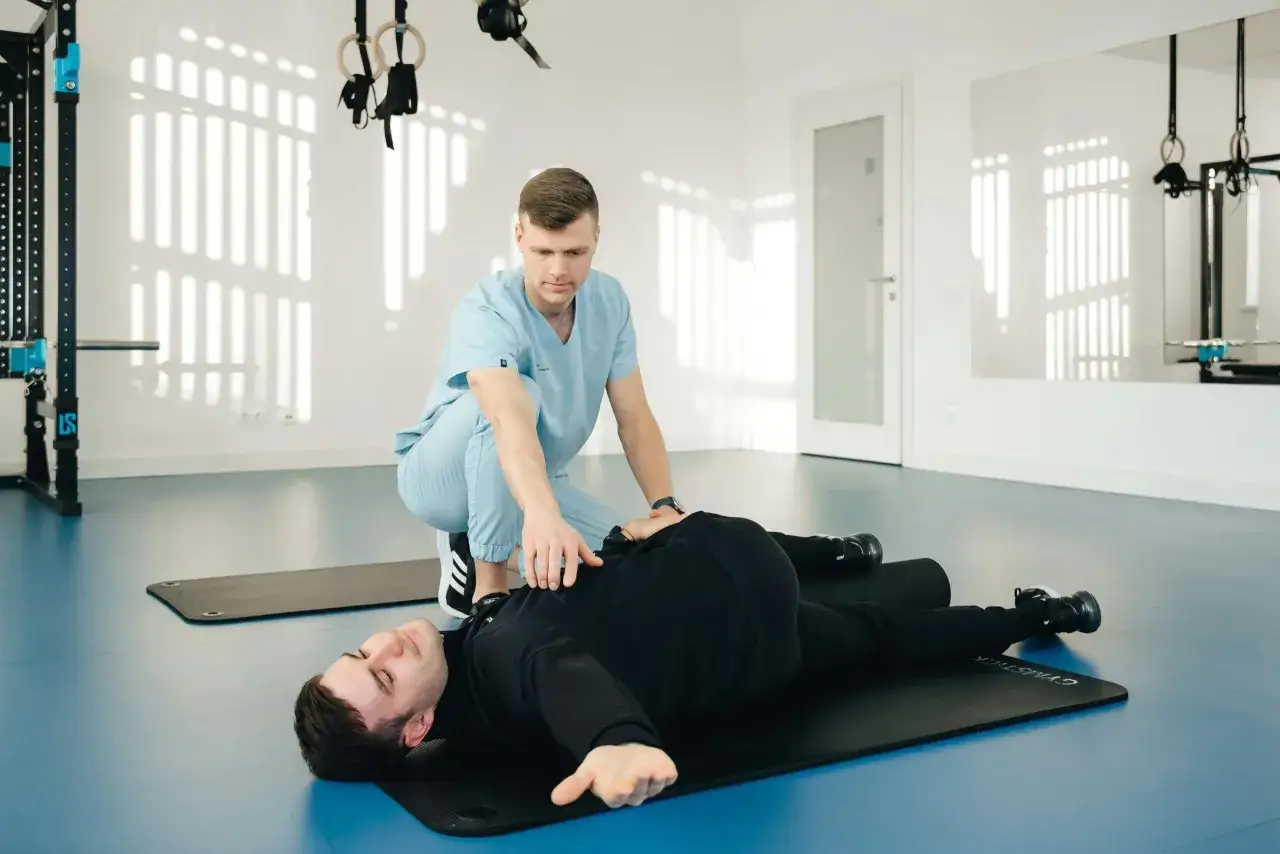 Fizjoterapeuta pomaga pacjentowi w ćwiczeniach na macie. To przykład, co to jest fizjoterapia: rehabilitacja i powrót do sprawności.