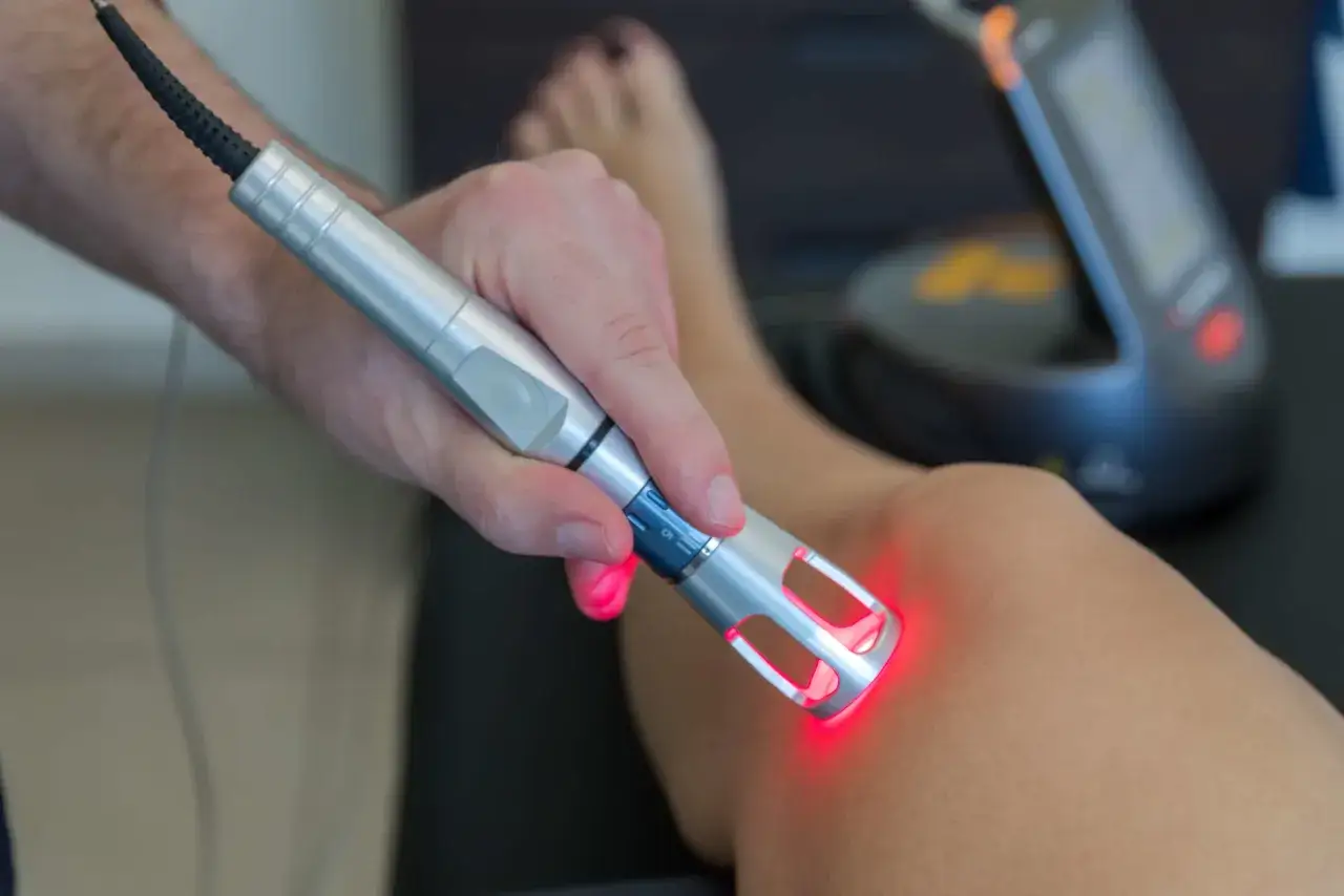 Terapeuta używa laser wysokoenergetyczny do zabiegu na kolanie pacjenta.