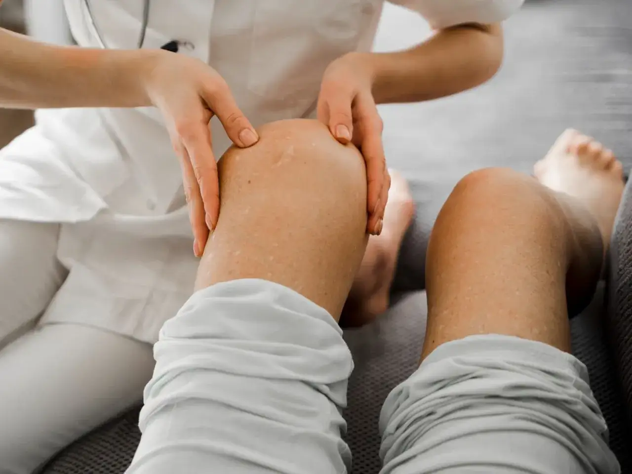 Fizjoterapeuta wykonuje ćwiczenia na drętwienie nóg od kręgosłupa, delikatnie dotykając kolana pacjenta.