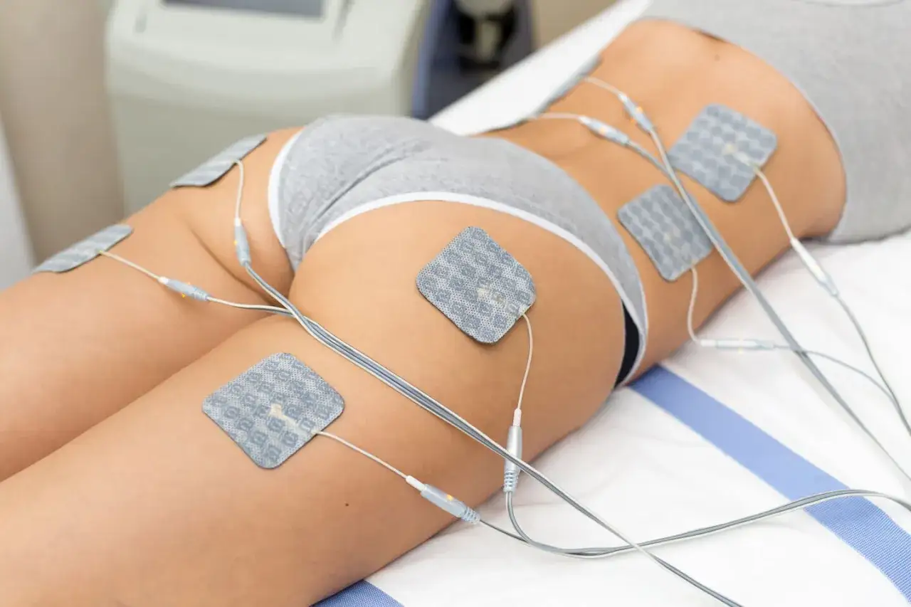 Elektrostymulacja mięśni (EMS) na udach i pośladkach. Elektrody podłączone do urządzenia, które ma pomóc w treningu.